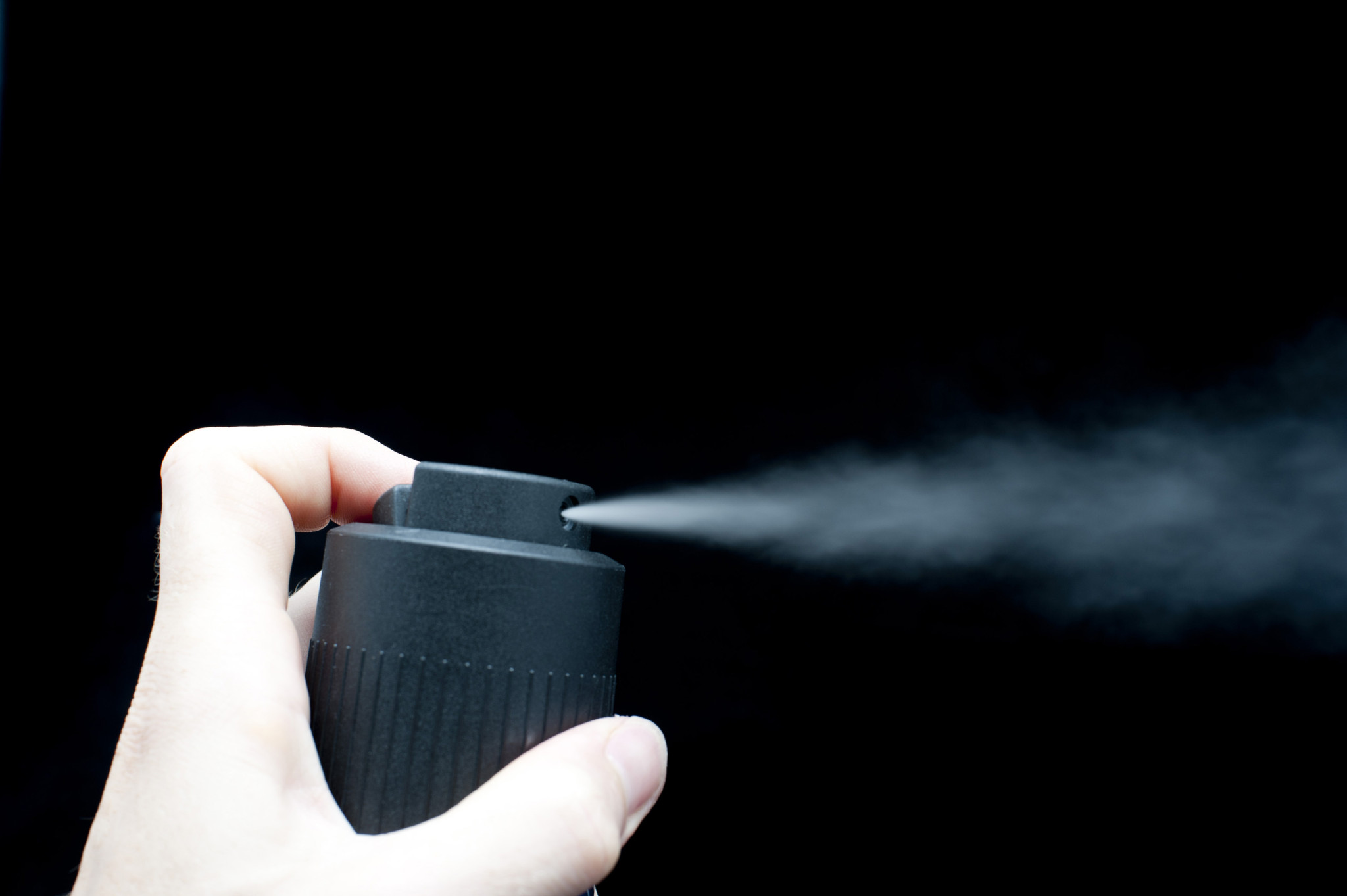 Close-up of hand holding a black can and spraying, black background