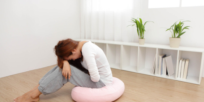 Portrait of woman with stomach ache sitting on floor at home asian model
