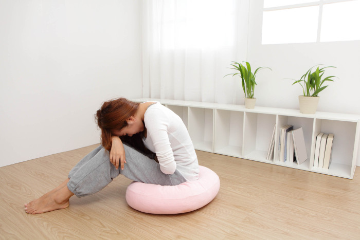 Portrait of woman with stomach ache sitting on floor at home asian model